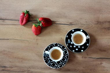 Düz bir atış iki fincan espresso ortaya çıkarır, her biri taze çilek eşliğinde, sade ahşap bir masa üzerine dizilmiş..