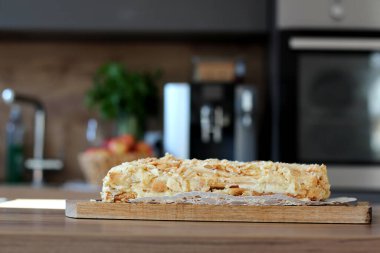 Nefis bir Napolyon keki, diğer adıyla mili-feuille, ahşap bir tahtanın üzerinde beyaz bir altlık üzerinde oturur, pullu tabakalarını, kremsi dolgusunu ve ufalanmış üstünü gösterir..
