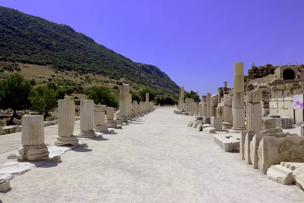 Fotoğrafta, tarihi bir arkeolojik alanı temsil eden, temiz bir gökyüzünün altında ayakta duran sütunları ve kırık taş yapıları bulunan antik kalıntılar sergileniyor..