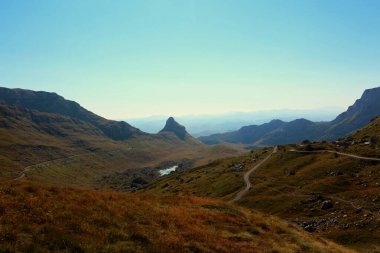 Görüntü, Karadağ 'ın Durmitor kentindeki berrak ve geniş mavi gökyüzünün altındaki vadiyi kesen dolambaçlı bir yol ile çarpıcı bir dağ manzarası yakalıyor.