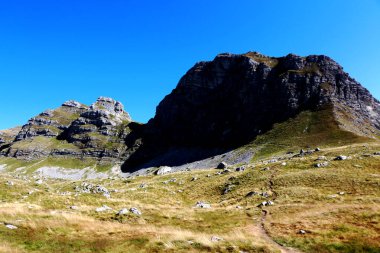 Görüntü, Karadağ 'ın Durmitor kentindeki berrak ve geniş mavi gökyüzünün altındaki vadiyi kesen dolambaçlı bir yol ile çarpıcı bir dağ manzarası yakalıyor.