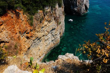 Sarp kayalıklar, küçük bir teknenin sürüklenerek Karadağ 'ın çarpıcı sahil güzelliğini ve engebeli doğal manzarasını sergilediği berrak turkuaz sulara dalıyor.