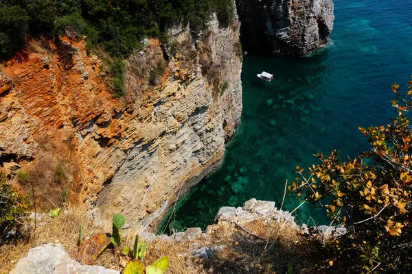 Sarp kayalıklar, küçük bir teknenin sürüklenerek Karadağ 'ın çarpıcı sahil güzelliğini ve engebeli doğal manzarasını sergilediği berrak turkuaz sulara dalıyor.