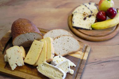 Köy ahşap bir tahtada, sağlıklı bir somun ekmek ve daha küçük bir tabak meyve ve ilave peynir dilimlerinin yanında çeşitli peynirler düzenlenir.