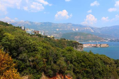 Canlı yeşil bir yamaç gök mavisi Adriyatik Denizi ile kesişiyor. Uçsuz bucaksız, parçalı bulutlu bir gökyüzü ve uzak dağların altındaki bir adada büyüleyici bir eski kasaba sergileniyor..