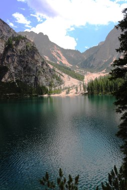 Etrafı engebeli dağlar ve yemyeşil ormanlarla çevrili sakin bir göl. Hepsi bulutlarla kaplı bir gökyüzünün altında. Temiz su çarpıcı manzarayı yansıtıyor..