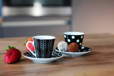 Tabaklar üzerinde iki şık kahve fincanı, taze kırmızı çilekler ve cazip çikolatalı mantarlarla birlikte ahşap bir yüzeye yerleştirilerek basit ama zarif bir hayat sahnesi oluşturulur..