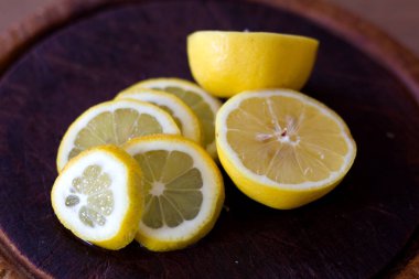 Yarım limonun yanına yerleştirilmiş canlı sarı limon dilimleri koleksiyonu. Sulu narenciye meyveleri kırsal, koyu ahşap bir tahtanın üzerinde oturur. Renk ve dokuda çarpıcı bir kontrastlık yaratır. Tazelik ve doğal güzelliği gösterir.