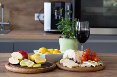 Yarım elma ve limon dilimleri olan ahşap bir tezgah ve başka bir tahtada da vişneli domatesli peynir. Bir saksı yeşil bitki ve bir bardak kırmızı şarap basit düzenlemelere biraz tazelik ve zarafet katar.