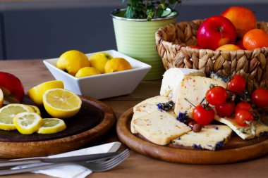 Kırsal tablolarda iki ahşap tahta bulunur: biri taze elma dilimleri, limonlar ve canlı kırmızı domatesler ve diğeri çeşitli peynir içerir. Bir sepet dokuma meyve ve yeşil saksı bitkisi renklendirici düzenlemelere eklenir.