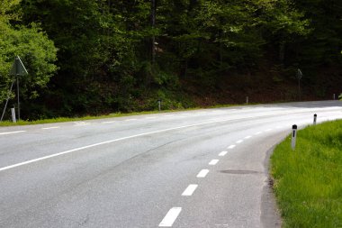 Virajlı boş asfalt yolu, açıkça beyaz çizgilerle işaretlenmiş, yoğun ağaçlarla dolu yeşil bir ortamda Avusturya Tyrol 'u andıran yol kenarında geziniyor..