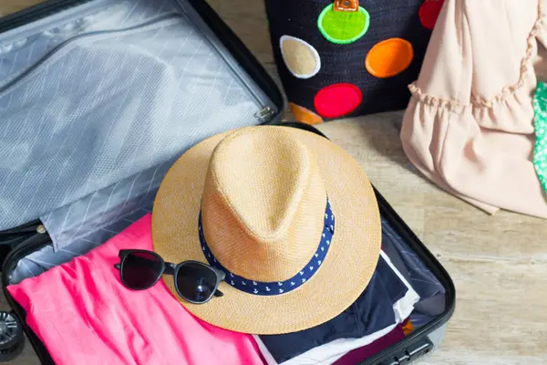Parlak elbiseler, hasır şapka ve güneş gözlükleri, yaklaşan bir yolculuk macerası için heyecanı yansıtan açık bir bavula dikkatlice yerleştirilmiştir..