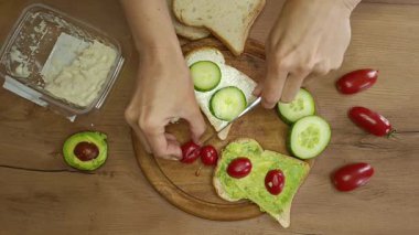 Canlı domatesler, salatalıklar, eller ustalıkla taze avokadolarla dolu lezzetli bir sandviç ve ahşap bir masada serpilmiş krema..