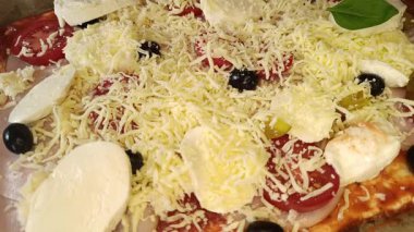 Mutfak ortamında hamuru, taze mozarellayı, zeytinleri, domatesleri ve otları kullanarak ağız sulandıran bir pizza hazırlar..