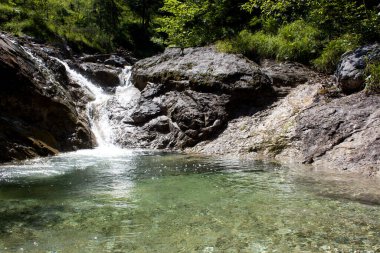 Su kayaların üzerinden yavaşça akar, huzurlu bir şelale oluşturur ve bu şelale sakin bir havuza boşalır. Alan canlı yeşilliklerle kaplıdır. Rahatlamak ve doğayı takdir etmek için idealdir..