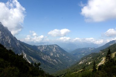 Bereketli yeşil vadiler ve görkemli dağ zirveleri kabarık bulutlu canlı mavi gökyüzünün altında uzanır. Sahne doğanın dinginliğini ve güzelliğini yakalar..