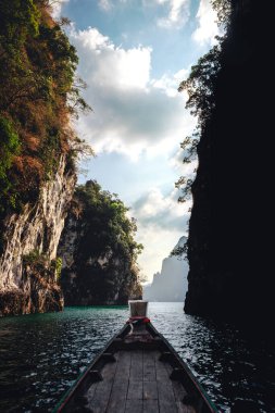 Güneşli bir günde, Khao Sok Ulusal Parkı 'ndaki Cheow Lan Gölü' nde yüksek kireçtaşı dağları arasında yüzen uzun teknenin güzel pruva manzarası, Tayland, Surat Thani.