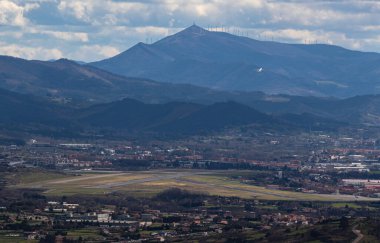 Arka planda Oiz Dağı tacı takılı Bilbao havaalanından kalkan uçağın yanı sıra Santurtzi, İspanya 'daki Serantes dağının tepesinden görülen bulutlu bir günde eski San Mames Stadyumu' nun kemeri görülüyor..