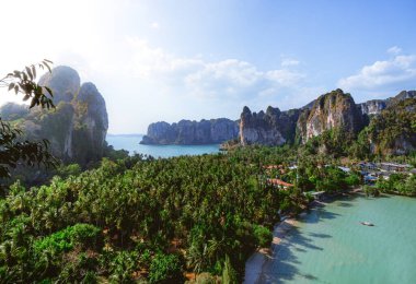 Tonsai Sahili 'nin arka planında palmiye ağaçları ve bitki örtüsüyle kaplı olan Railay Sahili' nin panoramik manzarası ve Tayland, Krabi 'de güneşli güzel bir günde kıyı boyunca yükselen kireç büyüklüğündeki dağlar..