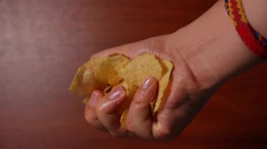 El, ahşap arka planda patates cipslerini sıkıca eziyor, doku, basınç ve insan yiyeceğiyle etkileşimini gösteriyor. Yüksek kalite 4k görüntü