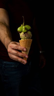 Fıstıklı ve çikolatalı dondurma külahını tutarken üstüne çikolata soslu üzümler dökülüyor, yaratıcı tatlı kompozisyonu. Yüksek kalite fotoğraf