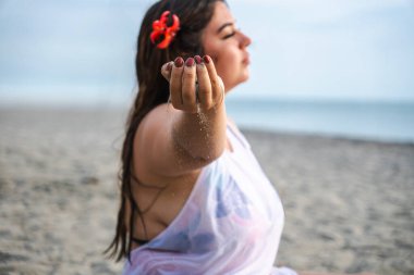 Gün batımında kumların ellerinden kayıp gitmesine izin veren iri yarı bir kadın. Yüksek kalite fotoğraf