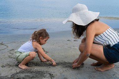 Anne ve kızı güneşli bir günde deniz kenarında kumsalda birlikte oynuyorlar. Yüksek kalite fotoğraf