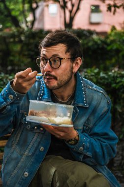 Hippi görünümlü beyaz bir adam öğle yemeğini dışarıda parkta bir beslenme çantasında yiyor. Açık havada yemek, huzur ve yaşam tarzı kavramı için. Yüksek kalite fotoğraf