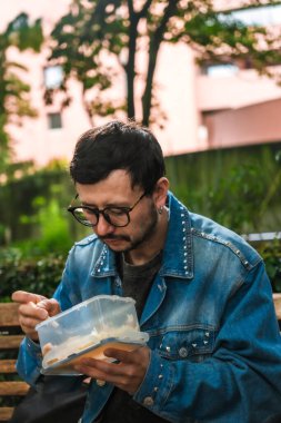 Hippi görünümlü beyaz bir adam öğle yemeğini dışarıda parkta bir beslenme çantasında yiyor. Açık havada yemek, huzur ve yaşam tarzı kavramı için. Yüksek kalite fotoğraf