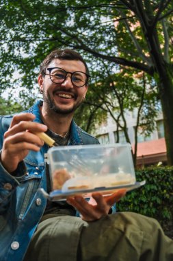 Hippi görünümlü beyaz bir adam öğle yemeğini dışarıda parkta bir beslenme çantasında yiyor. Açık havada yemek, huzur ve yaşam tarzı kavramı için. Yüksek kalite fotoğraf