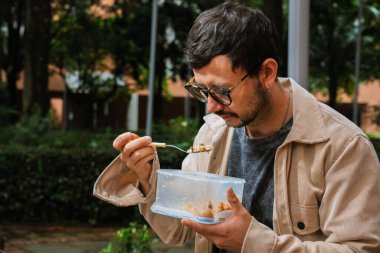 Hippi görünümlü beyaz bir adam öğle yemeğini dışarıda parkta bir beslenme çantasında yiyor. Açık havada yemek, huzur ve yaşam tarzı kavramı için. Yüksek kalite fotoğraf
