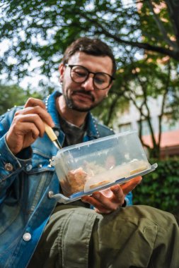 Hippi görünümlü beyaz bir adam öğle yemeğini dışarıda parkta bir beslenme çantasında yiyor. Açık havada yemek, huzur ve yaşam tarzı kavramı için. Yüksek kalite fotoğraf
