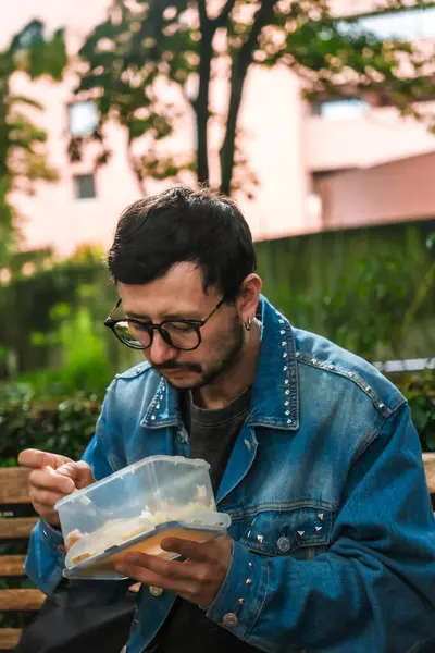 Hippi görünümlü beyaz bir adam öğle yemeğini dışarıda parkta bir beslenme çantasında yiyor. Açık havada yemek, huzur ve yaşam tarzı kavramı için. Yüksek kalite fotoğraf