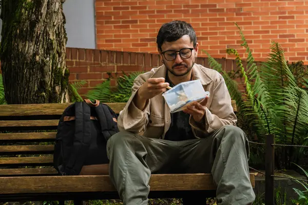 Hippi görünümlü beyaz bir adam öğle yemeğini dışarıda parkta bir beslenme çantasında yiyor. Açık havada yemek, huzur ve yaşam tarzı kavramı için. Yüksek kalite fotoğraf