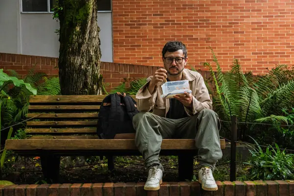 Hippi görünümlü beyaz bir adam öğle yemeğini dışarıda parkta bir beslenme çantasında yiyor. Açık havada yemek, huzur ve yaşam tarzı kavramı için. Yüksek kalite fotoğraf