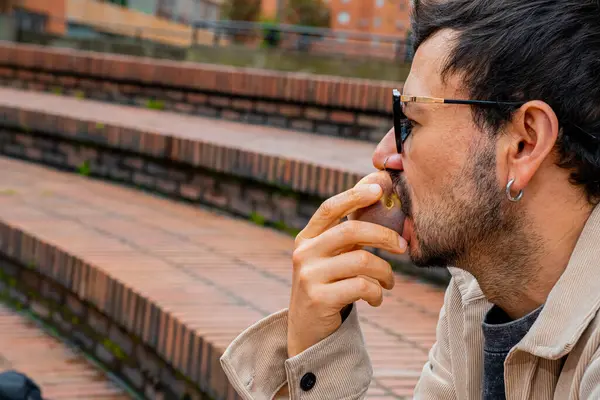 Elinde tuttuğu şeftaliyi ısıran sakallı ve gözlüklü bir adamın yakın plan görüntüsü şeftali ayı konsepti, sağlıklı yiyecekler, refah. Yüksek kalite fotoğraf