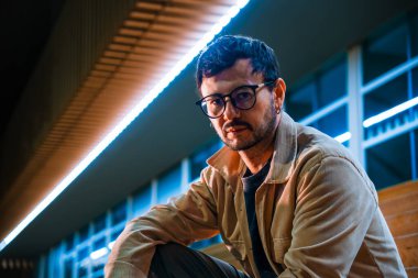 Merdivenlerde tek başına oturan genç bir adam gece hayatı ve moda konsepti için renkli ışıklarla Bogota 'da poz veriyor. Yüksek kalite fotoğraf