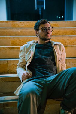 Merdivenlerde tek başına oturan genç bir adam gece hayatı ve moda konsepti için renkli ışıklarla Bogota 'da poz veriyor. Yüksek kalite fotoğraf