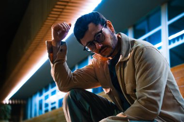 Merdivenlerde tek başına oturan genç bir adam gece hayatı ve moda konsepti için renkli ışıklarla Bogota 'da poz veriyor. Yüksek kalite fotoğraf