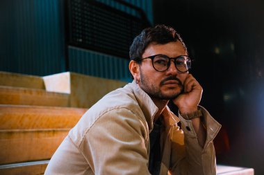 Merdivenlerde tek başına oturan genç bir adam gece hayatı ve moda konsepti için renkli ışıklarla Bogota 'da poz veriyor. Yüksek kalite fotoğraf