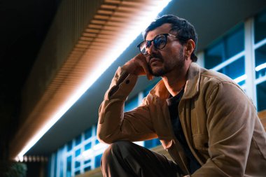 Merdivenlerde tek başına oturan genç bir adam gece hayatı ve moda konsepti için renkli ışıklarla Bogota 'da poz veriyor. Yüksek kalite fotoğraf