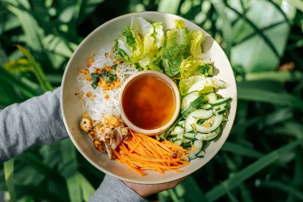 Dilimlenmiş salatalık, ızgara havuç ve pirinç eriştesiyle dolu nefis ev yapımı salata dolu bir kâse tutuyorum.