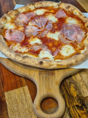 Tahta bir masada jambonlu, peynirli ve domatesli İtalyan pizzası