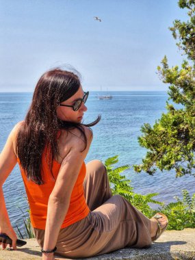 Deniz kenarındaki bir taşın üzerinde oturan kahverengi saçlı kadın. Güzel manzara. Deniz seti. Denizin zümrüt suyu