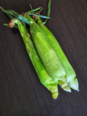 Ahşap arka planda yeşil kabuklarında üç taze mısır koçanı. Koçanda mısır.