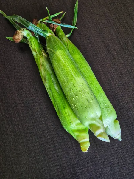 Ahşap arka planda yeşil kabuklarında üç taze mısır koçanı. Koçanda mısır.