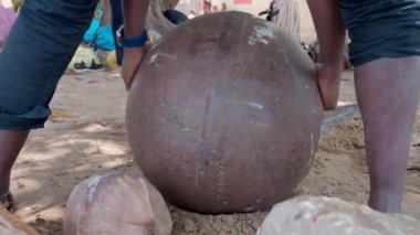 Afrikalı adam metal topla hindistan cevizi kırıyor.