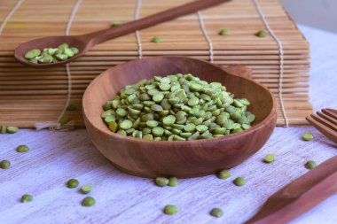 Kurumuş yeşil bezelyeler ahşap kasenin içinde. Suşi rulosunun yanında. Masanın üzerinde çatal ve tahta kaşıklar var.