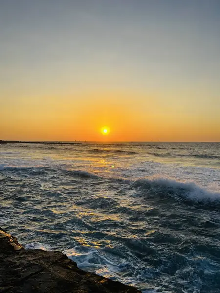 Akdeniz 'in üzerinde, Tel Aviv rıhtımında, yumuşak dalgalar ve canlı gökyüzü ile altın gün batımı.