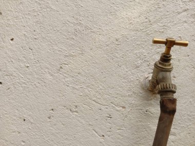Beyaz beton bir duvarda eski bir pirinç musluk. Metin için yeri olan bir boru hortumuna bağlı..